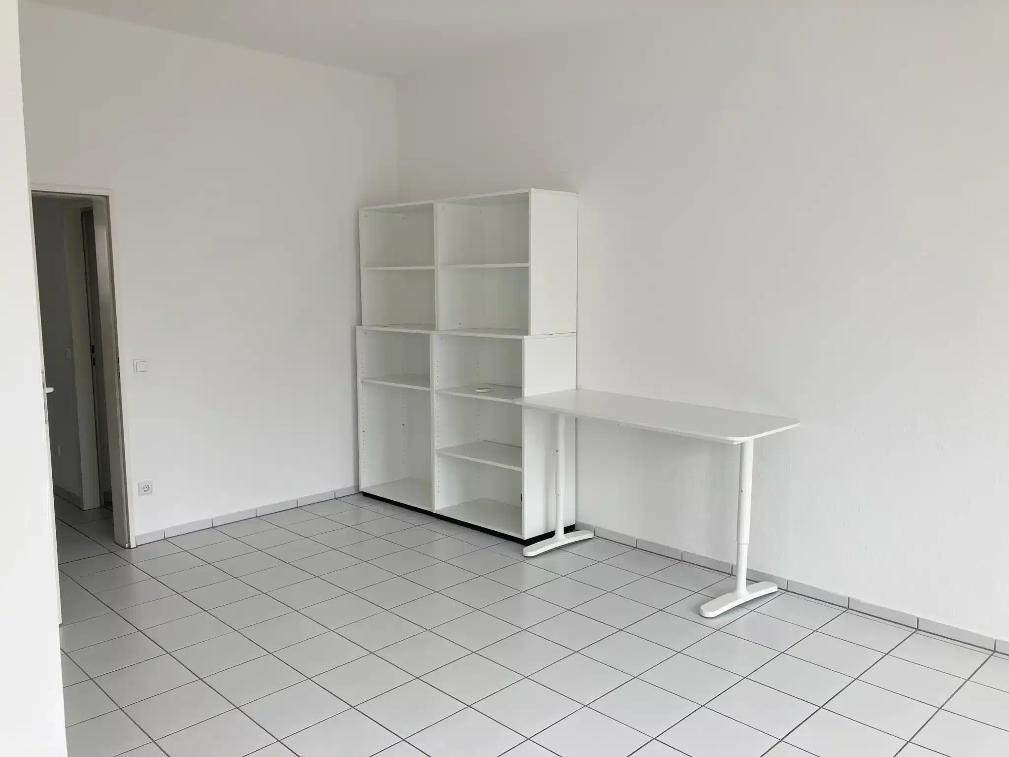 Leerer Büroraum mit weißen Regalen und Schreibtisch auf weiß gefliestem Boden.